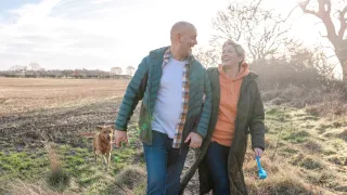 Couple walking outdoors with a dog, laughing.