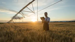 Farmer holding ipad standing next to irrigation pivot in a field