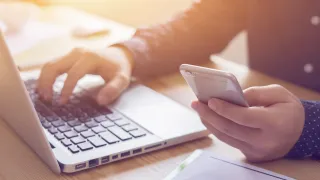 Person working on laptop and holding a phone.