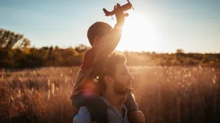 Father carrying son on shoulders, holding toy airplane.