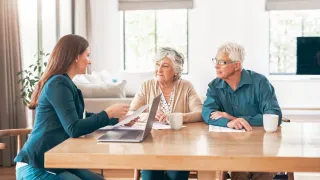 Elderly couple sitting at table receiving advice from young professional