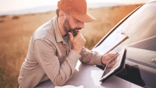 Farmer leaning on the hood of a truck using a tablet, golden hour