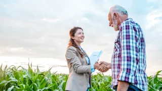 Older man shaking hands with a young woman in a field