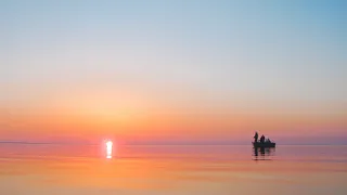 Sunset over calm water with a small boat.