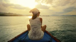 Woman in a boat looking at a sunset over the ocean.