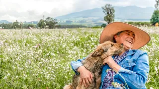 Woman in a field holding a dog while it licks her face