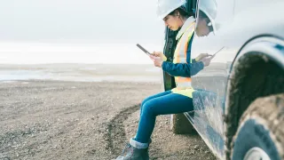 Labourer sitting on running board of vehicle while looking on their phone