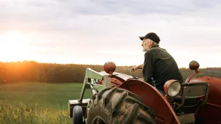 Farmer on a red tractor in a field at sunset.