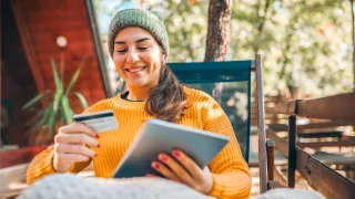 Woman sitting at table using a tablet and looking at credit card
