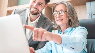 Young man in suit assisting woman using a laptop