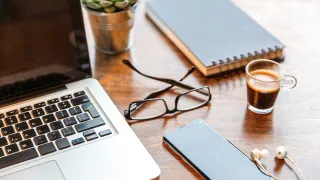 Laptop, phone, glasses and notebook on desk