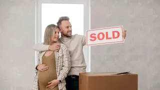 Pregnant couple, arm in arm, holding a "SOLD" sign.