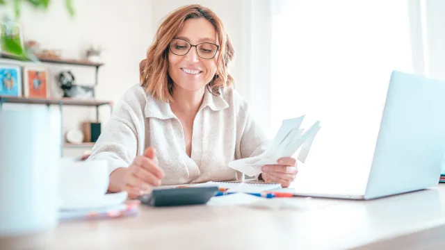 Woman in glasses working with a calculator and laptop.