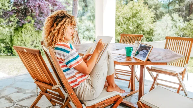 Woman sitting on wooden patio set, with a notebook and a tablet