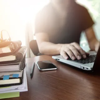 Man working on laptop at desk, with books and smartphone.