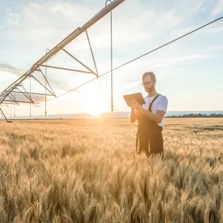 farmer standing in a field near an irrigation pivot, using a tablet