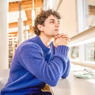Student in library leaning on a desk while thinking