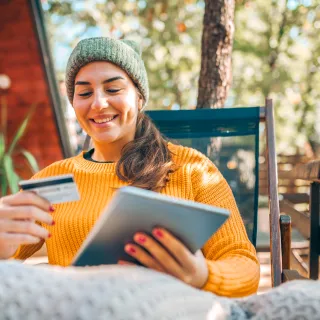 Woman sitting at table using a tablet and looking at credit card