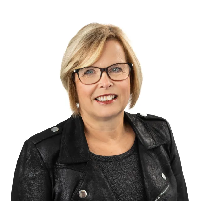 Blonde woman in glasses smiles, wearing a black jacket.
