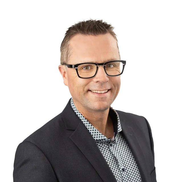 Man in a suit and glasses smiling, studio photograph.