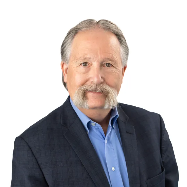 Portrait of a man in a blue shirt and navy suit jacket.