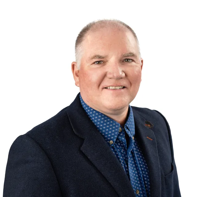 Headshot of a smiling man in a blue blazer and patterned shirt.