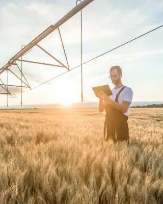 farmer standing in a field near an irrigation pivot, using a tablet